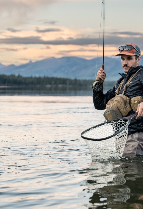 Man holds fly rod and net as he catches a trout.