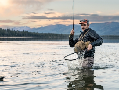 Man holds fly rod and net as he catches a trout.